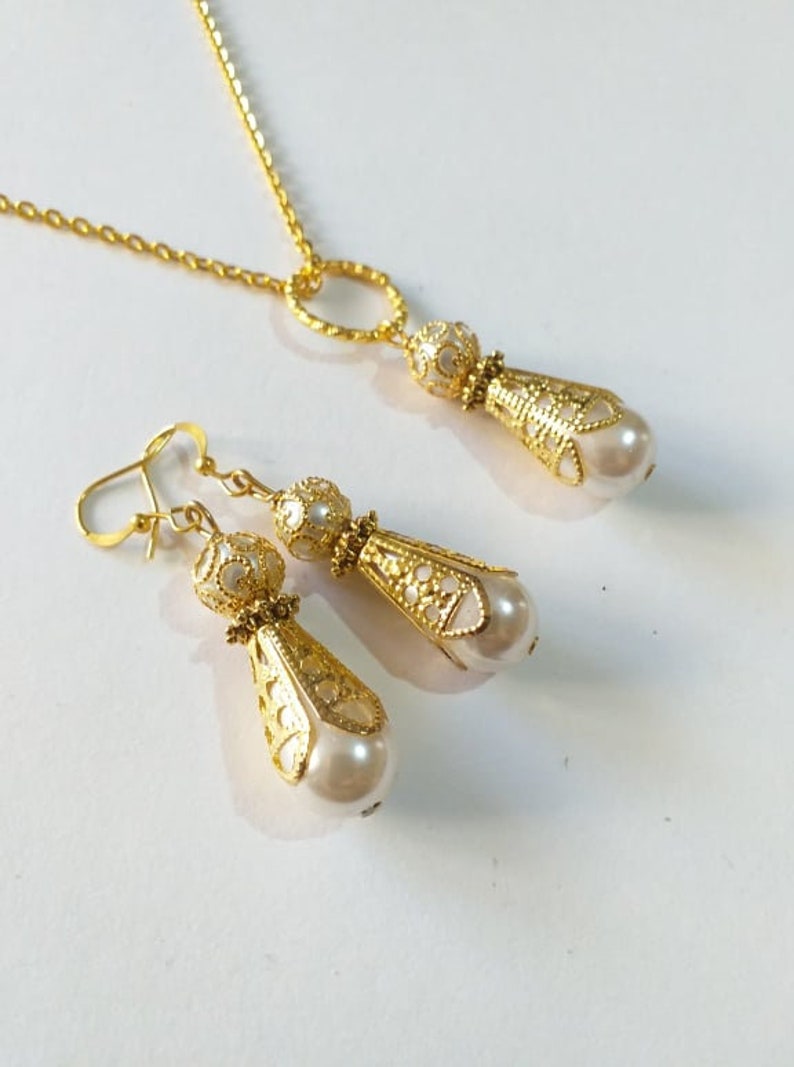 May include: A gold necklace and earrings set with a delicate chain and pearlescent teardrop pendants. The pendants feature intricate filigree designs.