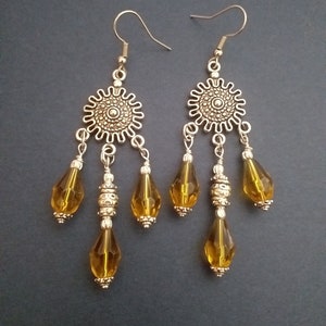 May include: A pair of dangle earrings with a silver tone finish. Each earring features a round, ornate charm with three teardrop-shaped amber glass beads hanging from it.