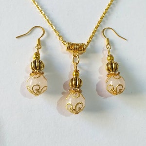 May include: A gold necklace and earrings set with a white stone pendant and matching earrings. The pendant and earrings feature a gold filigree design.