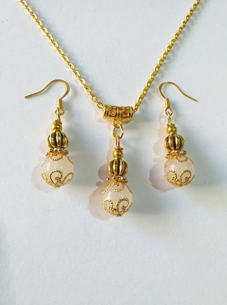 May include: A gold necklace and earrings set with a white stone pendant and matching earrings. The pendant and earrings feature a gold filigree design.