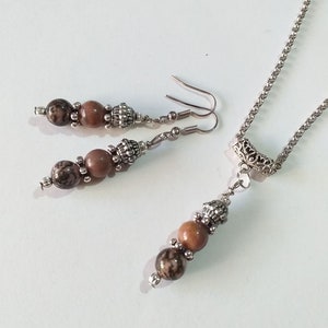 May include: A silver chain necklace with a pendant featuring three brown and black beads. Matching earrings with two brown and black beads hang from silver hooks.