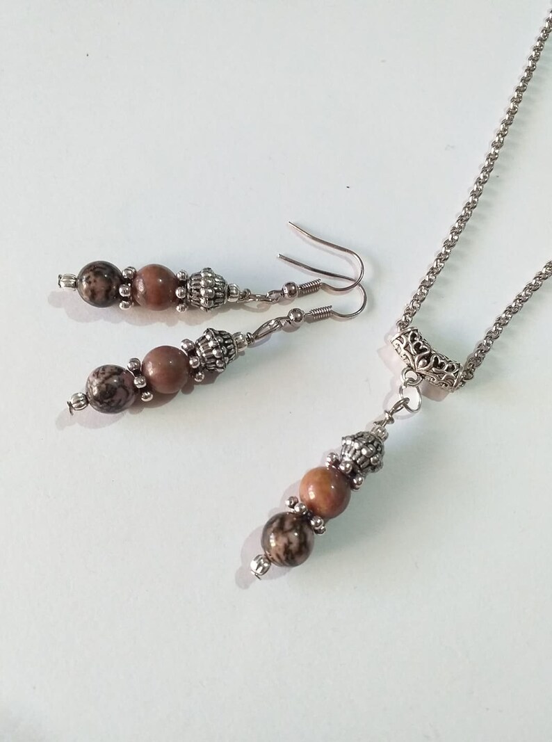May include: A silver chain necklace with a pendant featuring three brown and black beads. Matching earrings with two brown and black beads hang from silver hooks.