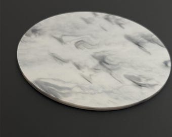 May include: A round, white coaster with a gray marbled pattern. The coaster is made of a smooth, hard material.