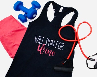 May include: A black racerback tank top with the text "WILL RUN FOR Wine" in white and pink, paired with coral leggings, blue dumbbells, and a red resistance band. Fitness and workout apparel.