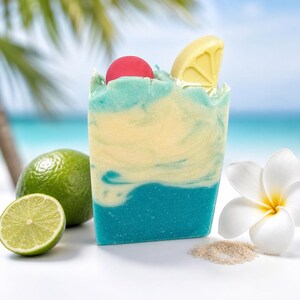 May include: A rectangular bar of soap featuring a marbled blend of light blue, cream, and dark blue colors. The top is decorated with a small red sphere and a yellow citrus wedge shape. The soap has a smooth, solid texture and a flat base.