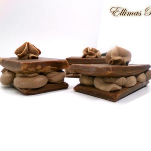 May include: Several chocolate pastries with layers of cream filling and a chocolate topping are arranged on a white surface. Each pastry has a decorative swirl of cream on top. The text "Ellima's Palm" is in the upper right corner.