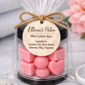 May include: A clear jar filled with pink mini lotion bars in various shapes, including squares, spheres, and hearts. The jar has a black lid and is tied with twine and a tag that reads "Ellima's Palm Mini Lotion Bars". Ingredients include coconut oil and shea butter.