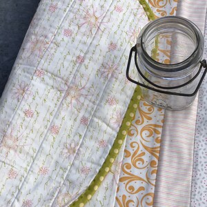 Puede incluir: Un mantel individual acolchado con un patr&oacute;n floral y un borde verde. El mantel individual est&aacute; doblado por la mitad y un frasco de vidrio est&aacute; encima.