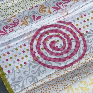 Puede incluir: Una colcha de retazos con un dise&ntilde;o en espiral rosa y blanco en el centro. La colcha est&aacute; hecha de diferentes telas con varios patrones, incluyendo lunares, dise&ntilde;os florales y escritura.