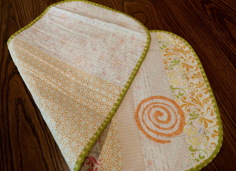 Puede incluir: Un camino de mesa acolchado con ribete verde y una variedad de patrones florales en tonos de amarillo, naranja y blanco.