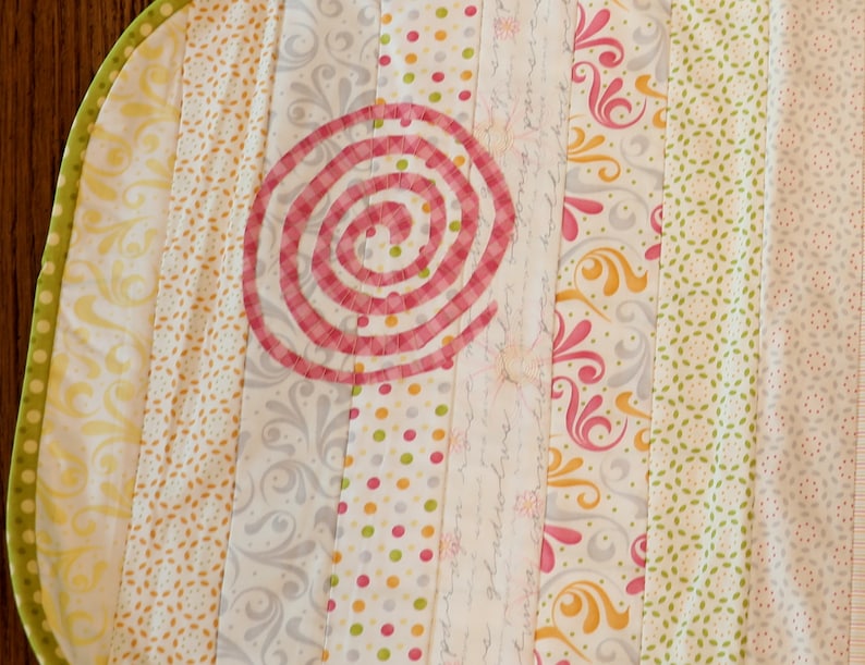 Puede incluir: Una colcha de retazos multicolor con un dise&ntilde;o en espiral rosa y blanco en el centro. La colcha est&aacute; hecha de varias telas con patrones florales, de lunares y geom&eacute;tricos.