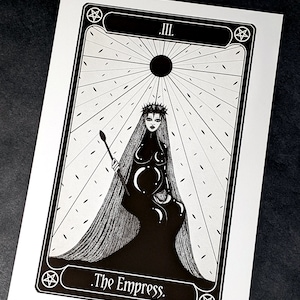 May include: Black and white tarot card illustration of The Empress, card number III. The Empress is depicted as a woman wearing a crown and a long flowing gown. She is holding a staff and a crescent moon.