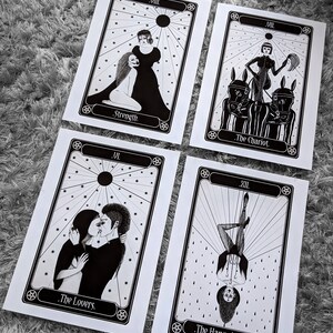 Może przedstawiać: Cztery karty tarota w czerni i bieli z ilustracjami Siły, Rydwanu, Zakochanych i Wisielca. Każda karta ma czarną ramkę i białe tło z czarnymi gwiazdami.