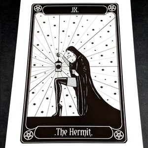 May include: Black and white illustration of The Hermit tarot card. The card features a woman in a hooded robe holding a lantern, with a pentagram in the corner. The text "IX. The Hermit." is at the bottom of the card.