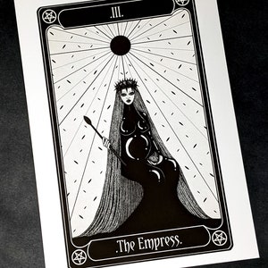 May include: Black and white tarot card illustration of The Empress, card number III. The Empress is depicted as a woman with a crown and long hair, sitting on a throne. She is holding a sceptre in her right hand and a globe in her left hand. The background is a white and black pattern.