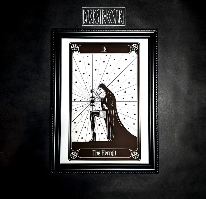 May include: A black and white illustration of The Hermit tarot card. The card features a hooded figure holding a lantern and standing in a field of stars. The card is framed in a black frame with a gold border.