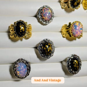 May include: A collection of vintage rings with oval-shaped stones. The rings feature gold and silver-toned settings with ornate details. Some stones are black with gold flecks, while others display iridescent colors.