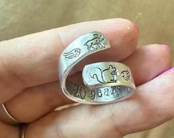 May include: A silver-colored spoon ring with a squirrel and wing design. The ring is engraved with the words "20 years". The ring is wrapped around the finger.