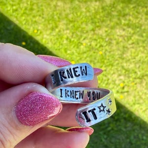 Puede incluir: Un anillo de metal plateado con dise&ntilde;o envolvente que presenta el texto negro grabado I KNEW I KNEW YOU IT junto a dos peque&ntilde;os s&iacute;mbolos de estrellas. El anillo tiene un dise&ntilde;o abierto y ajustable con un acabado liso y pulido.