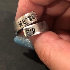 May include: A silver ring with the words "We're" and "F'd" engraved on it.