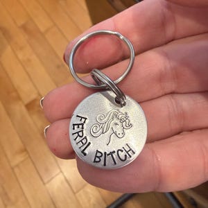 Puede incluir: Una taza de cerámica blanca con asa negra y el texto "But First, Coffee" en negrita negra. La taza se encuentra sobre un fondo borroso, sugiriendo un ambiente acogedor.