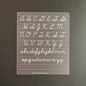 May include: A clear plastic sheet with white lines and the alphabet written in cursive. The letters are in uppercase and lowercase. The text at the bottom of the sheet reads "ByOurHandsDesigns.etsy.com".