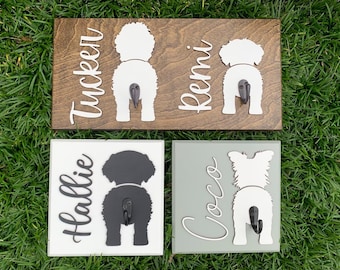 May include: Four wooden signs with dog silhouettes and names. The signs are in different colors and have black hooks. The names are "Tucker", "Remi", "Hallie", and "Coco".