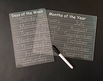 Peut inclure: Deux tableaux effaçables à sec en plastique transparent avec des lignes pointillées pour le traçage. Le tableau du haut porte le texte "Days of the Week" et liste les jours de la semaine. Le tableau du bas porte le texte "Months of the Year" et liste les mois de l'année. Un marqueur effaçable à sec blanc est à côté des tableaux.