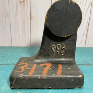 May include: A black wooden shoe last with the numbers "3-171" painted in orange on the base and "90A 779" stamped in black on the side.