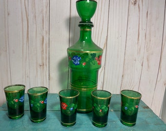 Puede incluir: Un juego de seis vasos de chupito de vidrio verde con ribetes dorados y diseños florales, y una jarra de vidrio verde a juego con un tapón dorado.