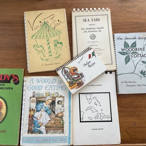 Könnte beinhalten: Eine Sammlung von Vintage-Kochbüchern mit bunten Umschlägen. Die Titel lauten "Mandy's Favorite Louisiana Recipes", "A World of Good Eating", "Variety Fair", "Sea Fare", "Italian Recipes", "Our Favorite Recipes Woodbine Cottage" und "The Harbor Sunapee, New Hampshire".