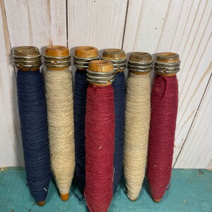 Peut inclure: Sept bobines de fil en bois, chacune avec un anneau m&eacute;tallique autour du haut. Les bobines sont envelopp&eacute;es de fils de diff&eacute;rentes couleurs&nbsp;: bleu, beige et rouge.