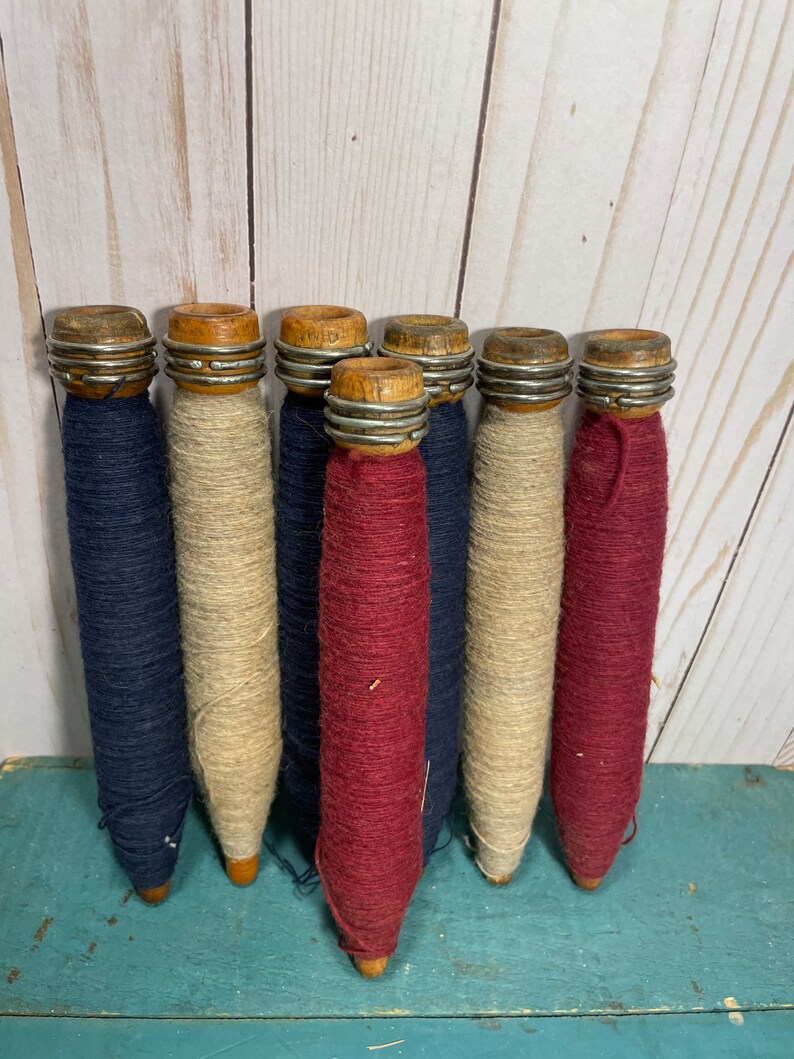 Peut inclure: Sept bobines de fil en bois, chacune avec un anneau m&eacute;tallique autour du haut. Les bobines sont envelopp&eacute;es de fils de diff&eacute;rentes couleurs&nbsp;: bleu, beige et rouge.