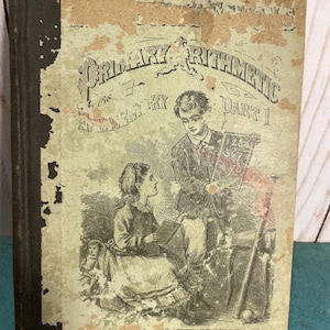 May include: An antique hardcover book titled Primary Arithmetic Part 1 with a worn, light green cover. The cover features a black and white illustration of a child holding a slate with numbers and another child sitting nearby, with a dark spine.