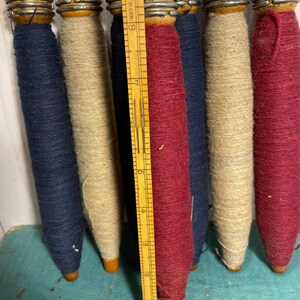 Peut inclure: Six bobines de fil en bois, chacune avec une couleur de fil diff&eacute;rente. Les bobines sont dispos&eacute;es en rang&eacute;e, avec une r&egrave;gle derri&egrave;re elles. Les couleurs du fil sont bleu marine, beige, bordeaux, bleu marine, beige et bordeaux.