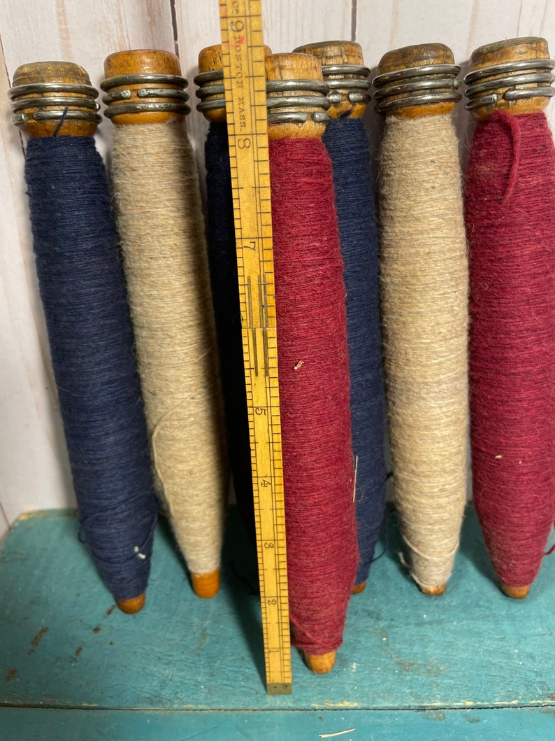 Peut inclure: Six bobines de fil en bois, chacune avec une couleur de fil diff&eacute;rente. Les bobines sont dispos&eacute;es en rang&eacute;e, avec une r&egrave;gle derri&egrave;re elles. Les couleurs du fil sont bleu marine, beige, bordeaux, bleu marine, beige et bordeaux.