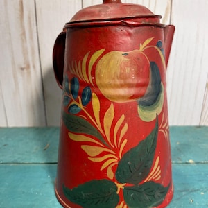 May include: Red metal teapot with a painted floral design featuring green leaves, yellow flowers, and red apples. The teapot has a lid and a handle.