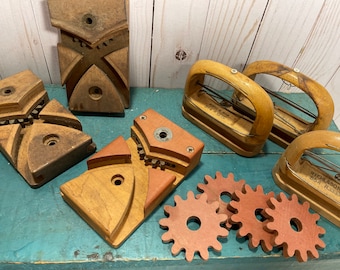 Peut inclure: Un ensemble d'outils en bois anciens, comprenant un jeu de quatre blocs en bois avec des engrenages et une paire d'étriers en bois avec un fil métallique. Les outils sont sur une surface bleue avec un fond en bois. Les étriers portent l'inscription "HIGHLASON 654 R3333".