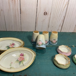 Könnte beinhalten: Set aus vier antiken Salz- und Pfefferstreuern aus Porzellan mit Blumendesigns. Die Streuer sind weiß mit blauen und rosa Akzenten. Es gibt auch vier kleine, runde Porzellanschalen in rosa, grün und blau.