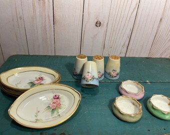 May include: Set of four vintage porcelain salt and pepper shakers with floral designs. The shakers are white with blue and pink accents. There are also four small, round, porcelain dishes in pink, green, and blue.