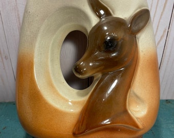 Może przedstawiać: Ceramiczny wazon z brązową i białą glazurą przedstawiający motyw głowy jelenia. Wazon ma duży otwór i zaokrąglone dno.
