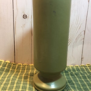 Pode incluir: Um vaso de cerâmica verde alto com uma base larga. O vaso tem um acabamento liso e brilhante.