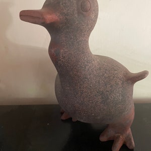 May include: A brown ceramic bird figurine with a textured surface and a small, round eye. The bird has a long neck and a small beak. The figurine is standing on a black surface.
