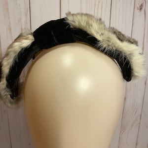 May include: A black velvet headband with a faux fur trim. The headband is on a mannequin head.