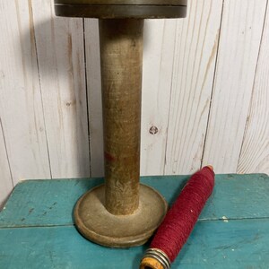Peut inclure: Une bobine en bois avec une pelote de fil rouge. La bobine a une base large et un centre cylindrique haut. Le fil est enroul&eacute; autour d'une petite bobine en bois.