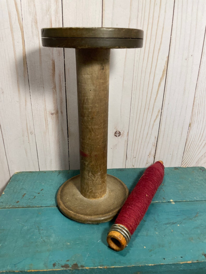 Peut inclure: Une bobine en bois avec une pelote de fil rouge. La bobine a une base large et un centre cylindrique haut. Le fil est enroul&eacute; autour d'une petite bobine en bois.