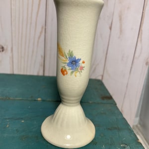 Könnte beinhalten: Eine cremefarbene Vintage-Keramikvase mit Deckel, verziert mit einem Blumendesign mit blauen und rosa Blüten, Weizen und orangefarbenen Akzenten. Die Vase hat eine Craquelé-Glasur und einen ausgestellten Sockel.