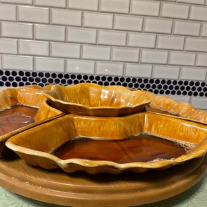 May include: A brown ceramic serving dish with four individual bowls. The dish is on a wooden base and has a scalloped edge.
