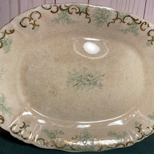 May include: An oval serving platter with a white background and a green and gold floral design around the edge.