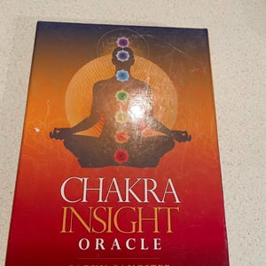 May include: A Chakra Insight Oracle card deck with a colorful illustration of a meditating figure with chakra symbols. The box has a gradient background of orange, red, and blue with the title "Chakra Insight Oracle" and the author's name.